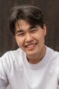Cheerful young man with a toothy smile wearing a white t-shirt and posing confidently outdoors.